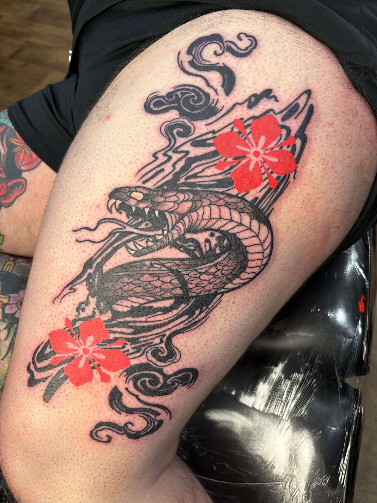 Tattoo of a Japanese style snake with red flowers on a leg
delboitattoos 